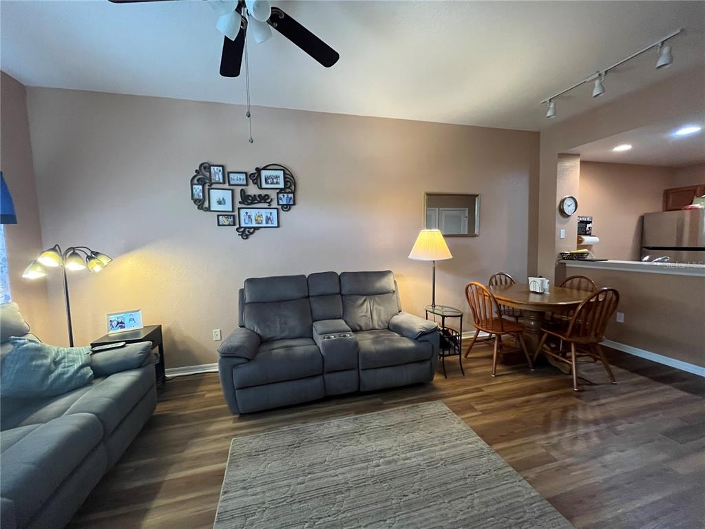 A living room with wood-look flooring, a grey loveseat, a dining set, and wall decor — 2610 LODI CIRCLE UNIT 103, KISSIMMEE, FL