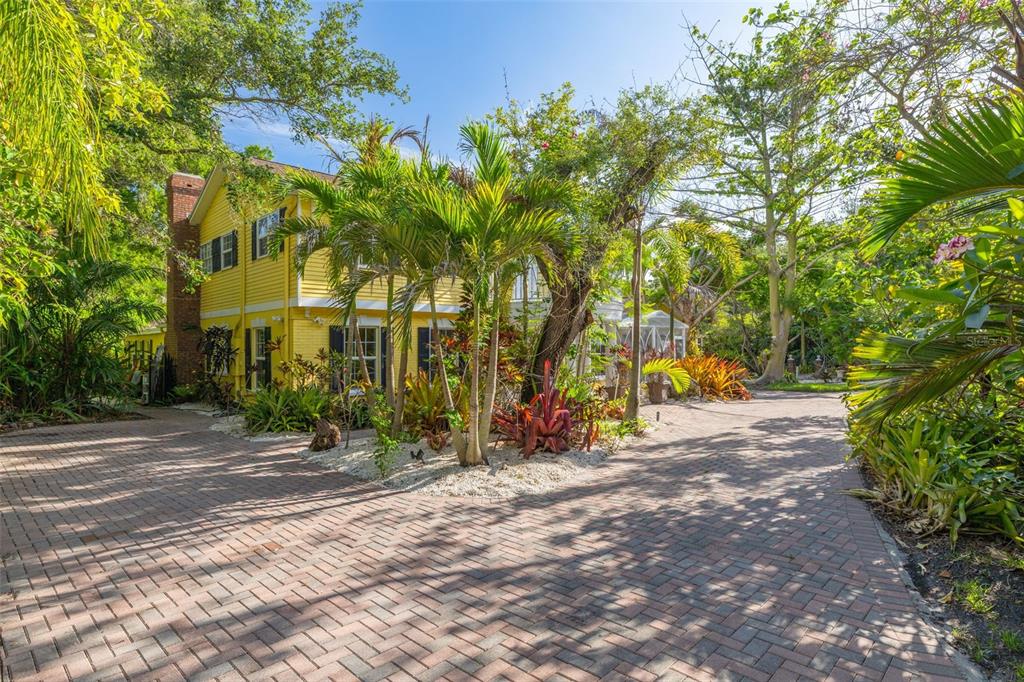 A yellow two-story house with a brick driveway surrounded by lush tropical landscaping — 1821 OAK CREEK DRIVE, DUNEDIN, FL