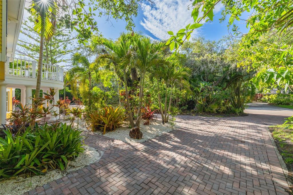 A brick driveway leads to a house with a white balcony and lush tropical landscaping — 1821 OAK CREEK DRIVE, DUNEDIN, FL