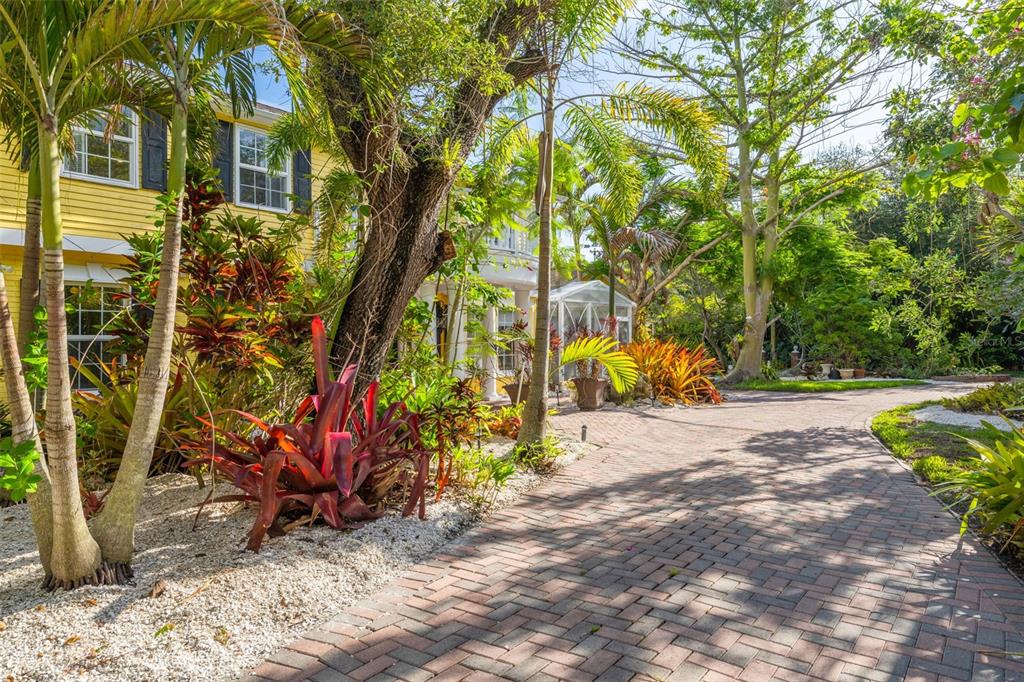 A brick driveway leads to a yellow house surrounded by lush tropical landscaping and trees — 1821 OAK CREEK DRIVE, DUNEDIN, FL