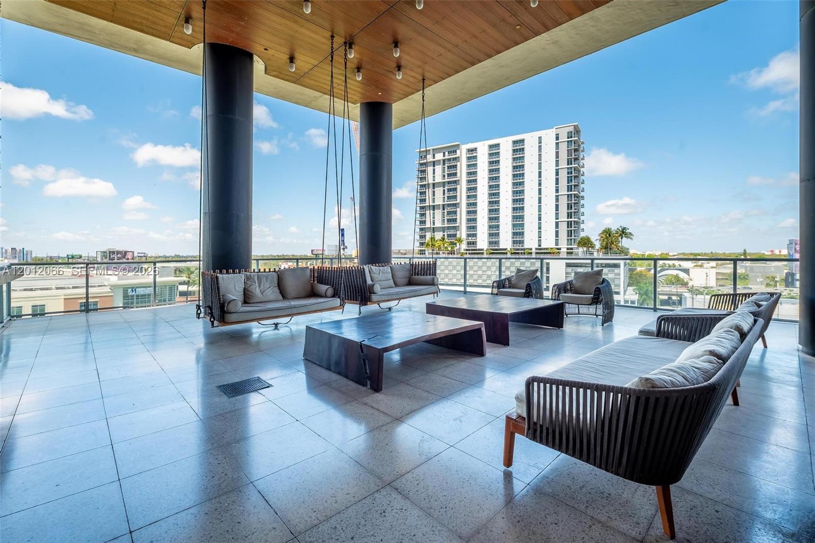 A spacious outdoor balcony features hanging sofas, modern furniture, and views of nearby buildings — 3470 E Coast Ave # H0302, Miami FL 33137, MIAMI, FL