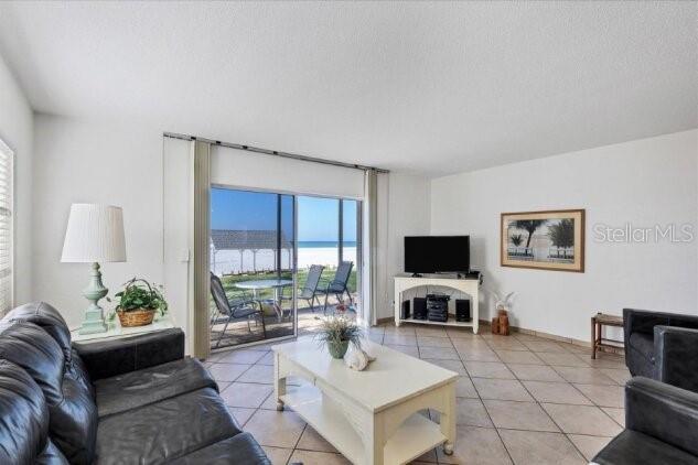 A living room with tile floors, a leather sofa, and a sliding door to the beach — 6154 MIDNIGHT PASS ROAD UNIT 101, SARASOTA, FL