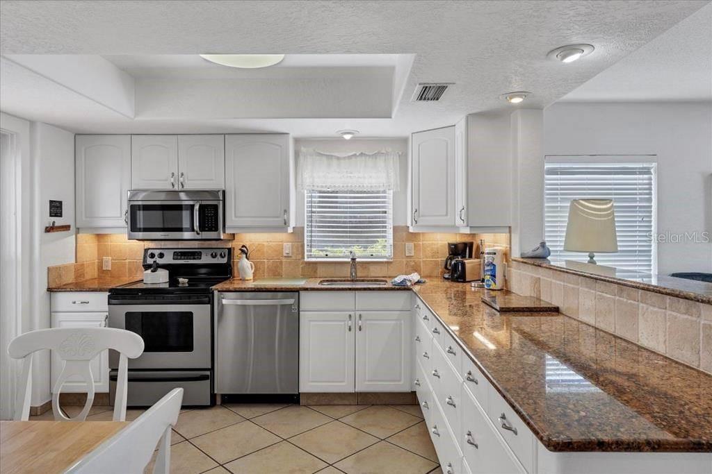 A kitchen features white cabinetry, granite countertops, stainless steel appliances, and tiled flooring — 6154 MIDNIGHT PASS ROAD UNIT 101, SARASOTA, FL