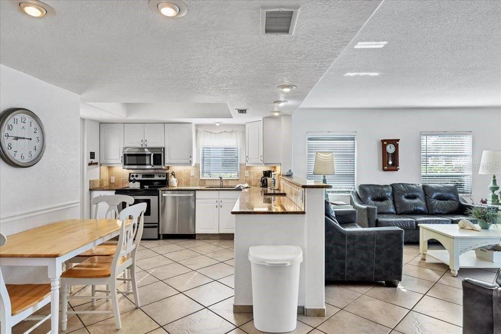 An open-concept kitchen with white cabinets and tile floors connects to a living room area — 6154 MIDNIGHT PASS ROAD UNIT 101, SARASOTA, FL