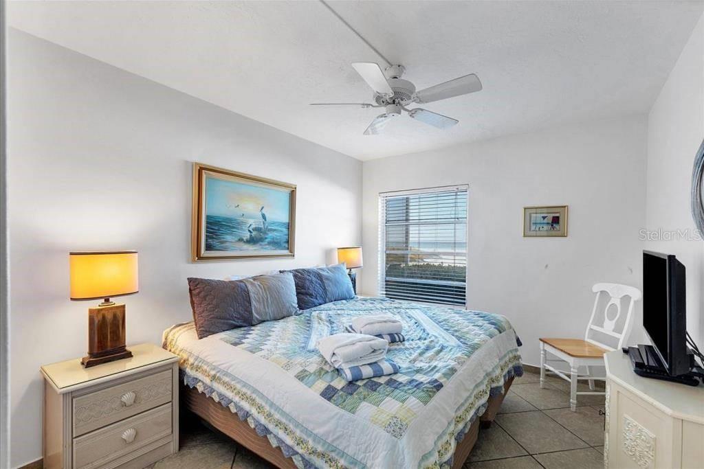 A bedroom features a bed with a blue quilt, a ceiling fan, and a window — 6154 MIDNIGHT PASS ROAD UNIT 101, SARASOTA, FL