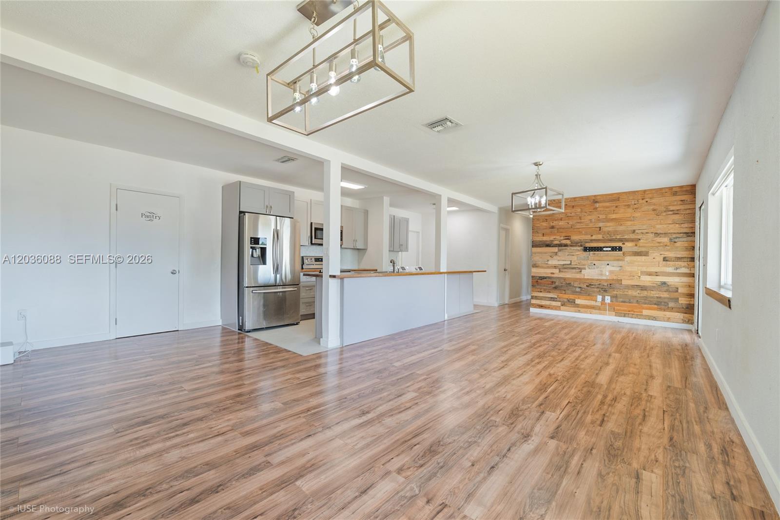 An open-concept living and kitchen area features wood-look flooring and a rustic wood-paneled wall — 11601 SW 141st St, Miami FL 33176, MIAMI, FL
