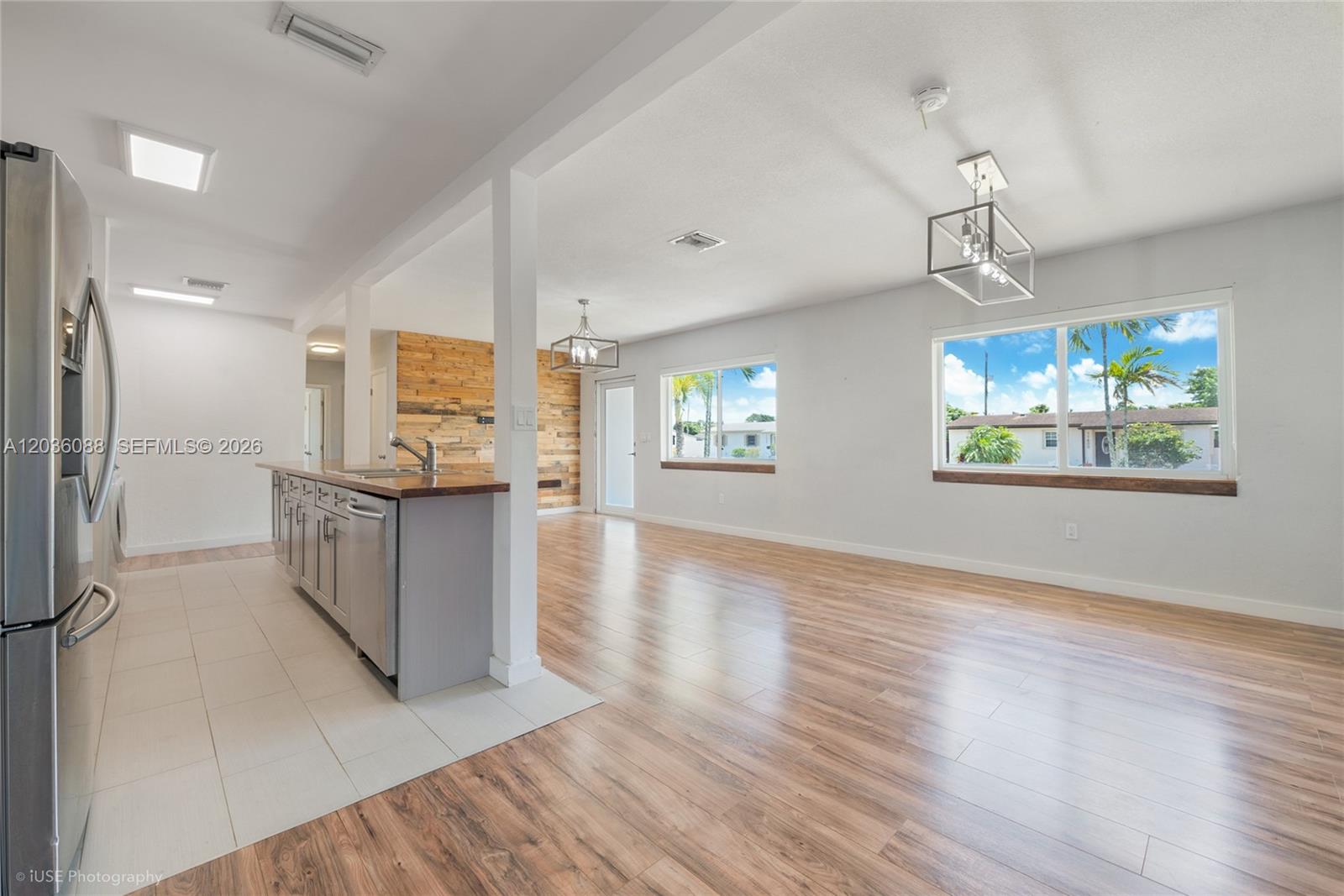 An open-concept kitchen and living area features wood-look flooring, a wood-paneled accent wall, and windows — 11601 SW 141st St, Miami FL 33176, MIAMI, FL