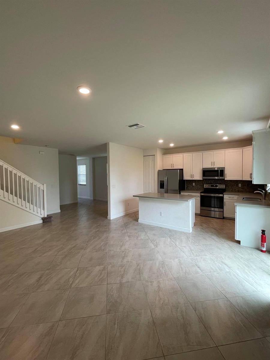 An open-concept kitchen and living area featuring tile flooring, white cabinetry, and stainless steel appliances — 12932 Anthorne Lane, Boynton Beach FL 33436, BOYNTON BEACH, FL