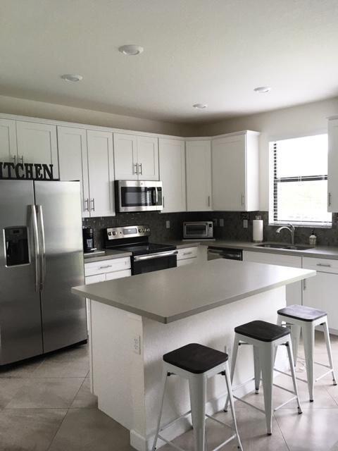 A kitchen features white cabinetry, stainless steel appliances, a gray island, and three bar stools — 12932 Anthorne Lane, Boynton Beach FL 33436, BOYNTON BEACH, FL