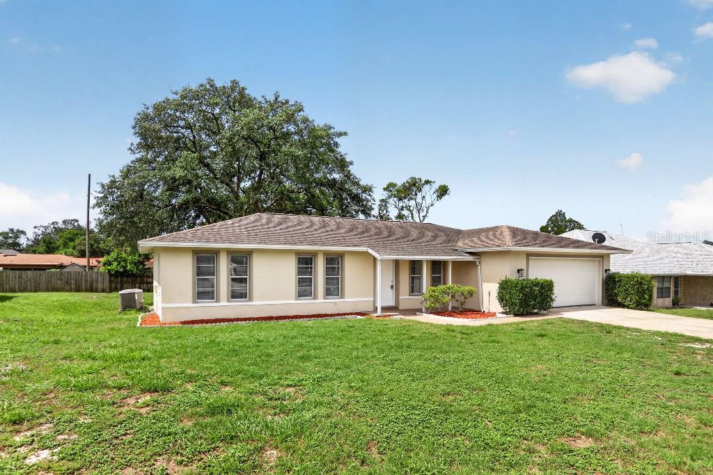 A single-story house with a tan exterior, a white garage door, and a large tree — 1013 SULLIVAN STREET, DELTONA, FL