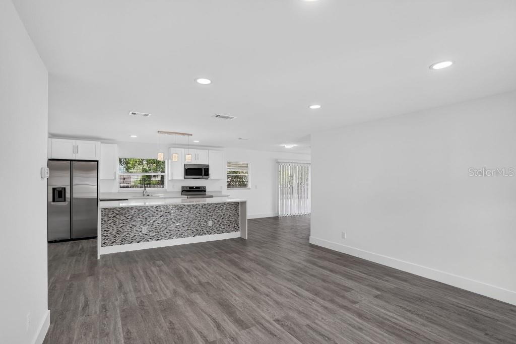 A modern kitchen with white cabinets and a mosaic-tiled island opens to a living area — 1013 SULLIVAN STREET, DELTONA, FL