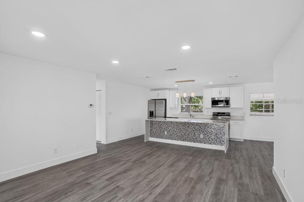 A modern kitchen with white cabinets and a mosaic-tiled island opens to a living area — 1013 SULLIVAN STREET, DELTONA, FL