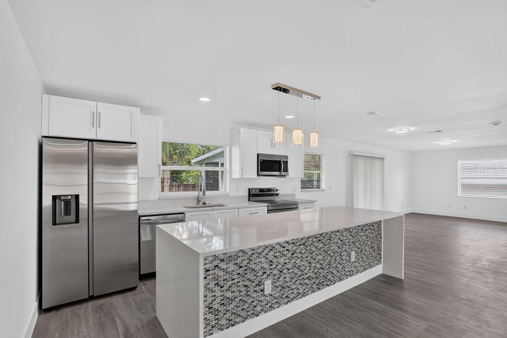 A modern kitchen features white cabinets, stainless steel appliances, and a stone-tiled kitchen island — 1013 SULLIVAN STREET, DELTONA, FL