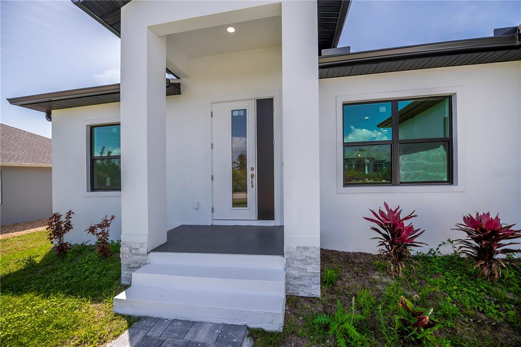 The exterior of a modern white house features a covered entryway with stone accents — 15089 ALDAMA CIRCLE, PORT CHARLOTTE, FL