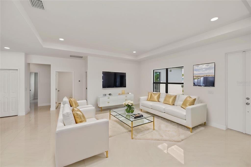 A bright living room features white sofas, a glass coffee table, and a wall-mounted television — 15089 ALDAMA CIRCLE, PORT CHARLOTTE, FL