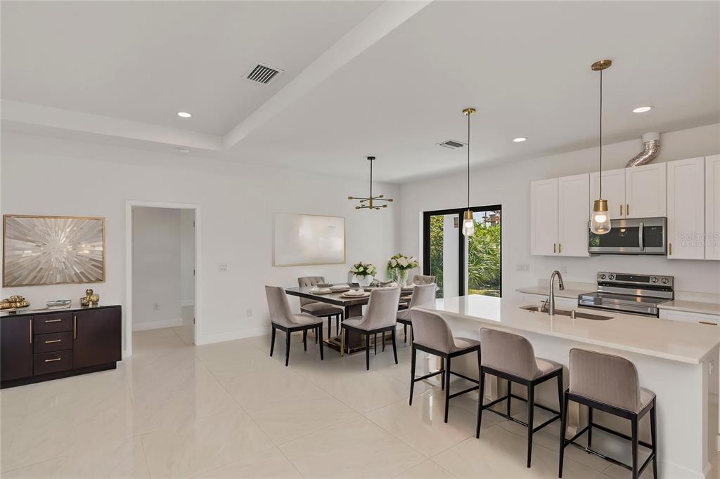 An open-concept kitchen and dining area features white cabinetry, quartz countertops, and tile flooring — 15089 ALDAMA CIRCLE, PORT CHARLOTTE, FL