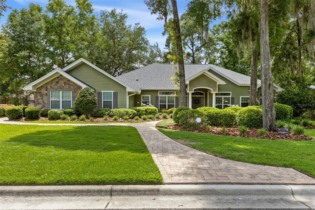 A single-story green house with stone accents, a paved walkway, and mature trees — 3782 SW 105TH STREET, GAINESVILLE, FL