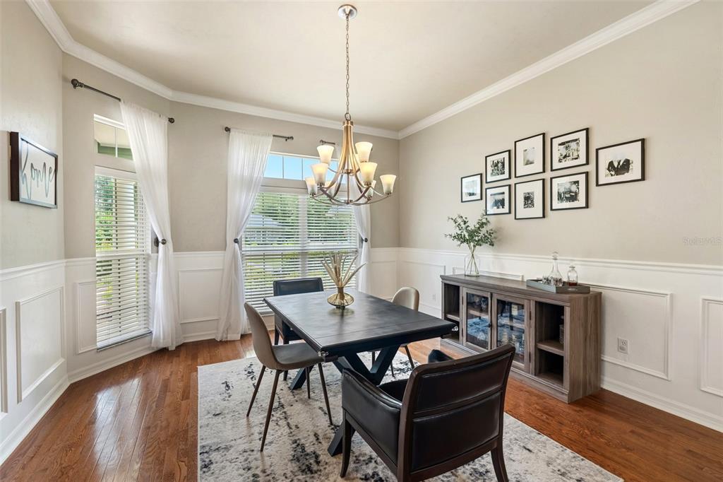 A dining room features a dark wood table, a chandelier, wainscoting, and a gallery wall — 3782 SW 105TH STREET, GAINESVILLE, FL
