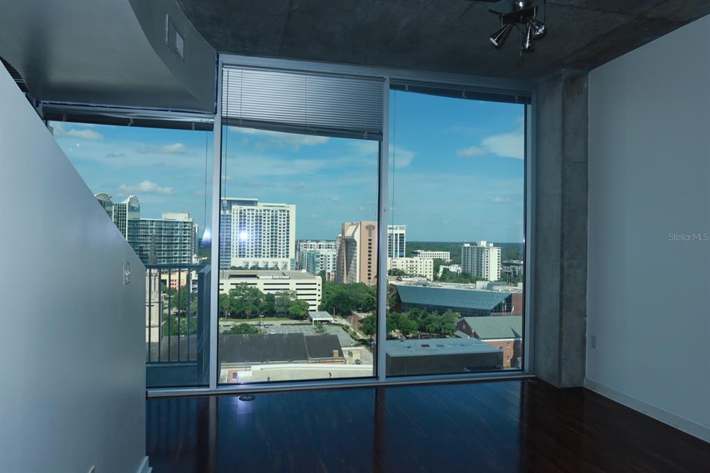 An empty room with dark hardwood floors and floor-to-ceiling windows overlooking a city skyline — 155 S COURT AVENUE UNIT 1113, ORLANDO, FL
