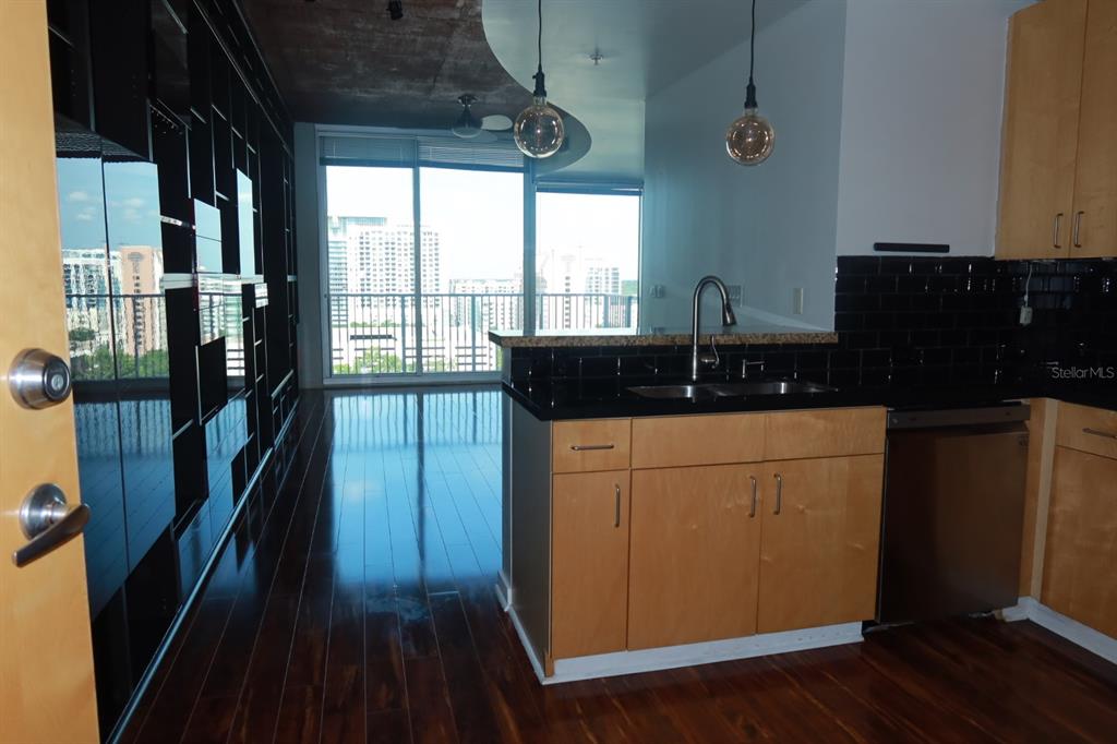 A kitchen with light wood cabinets and black tile backsplash overlooks a living area with floor-to-ceiling windows — 155 S COURT AVENUE UNIT 1113, ORLANDO, FL