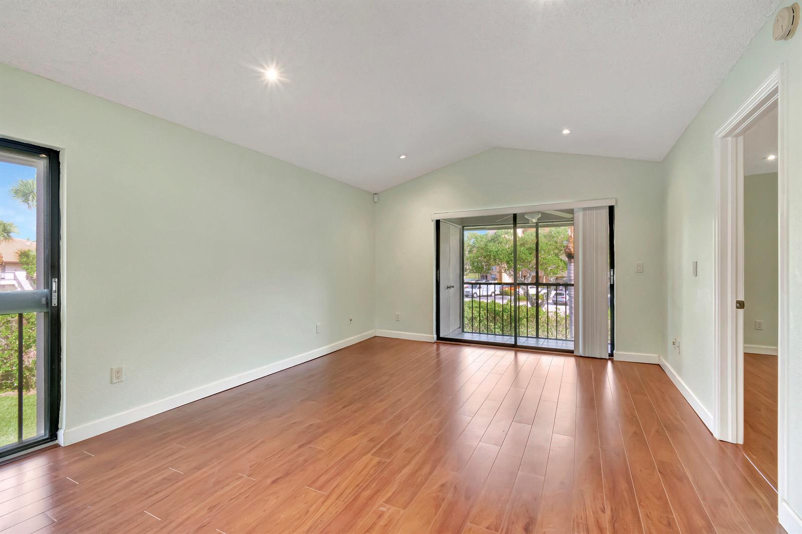 An empty room with light green walls, wood-look flooring, and two sliding glass balcony doors — 351 Club Circle # 207, Boca Raton FL 33487, BOCA RATON, FL