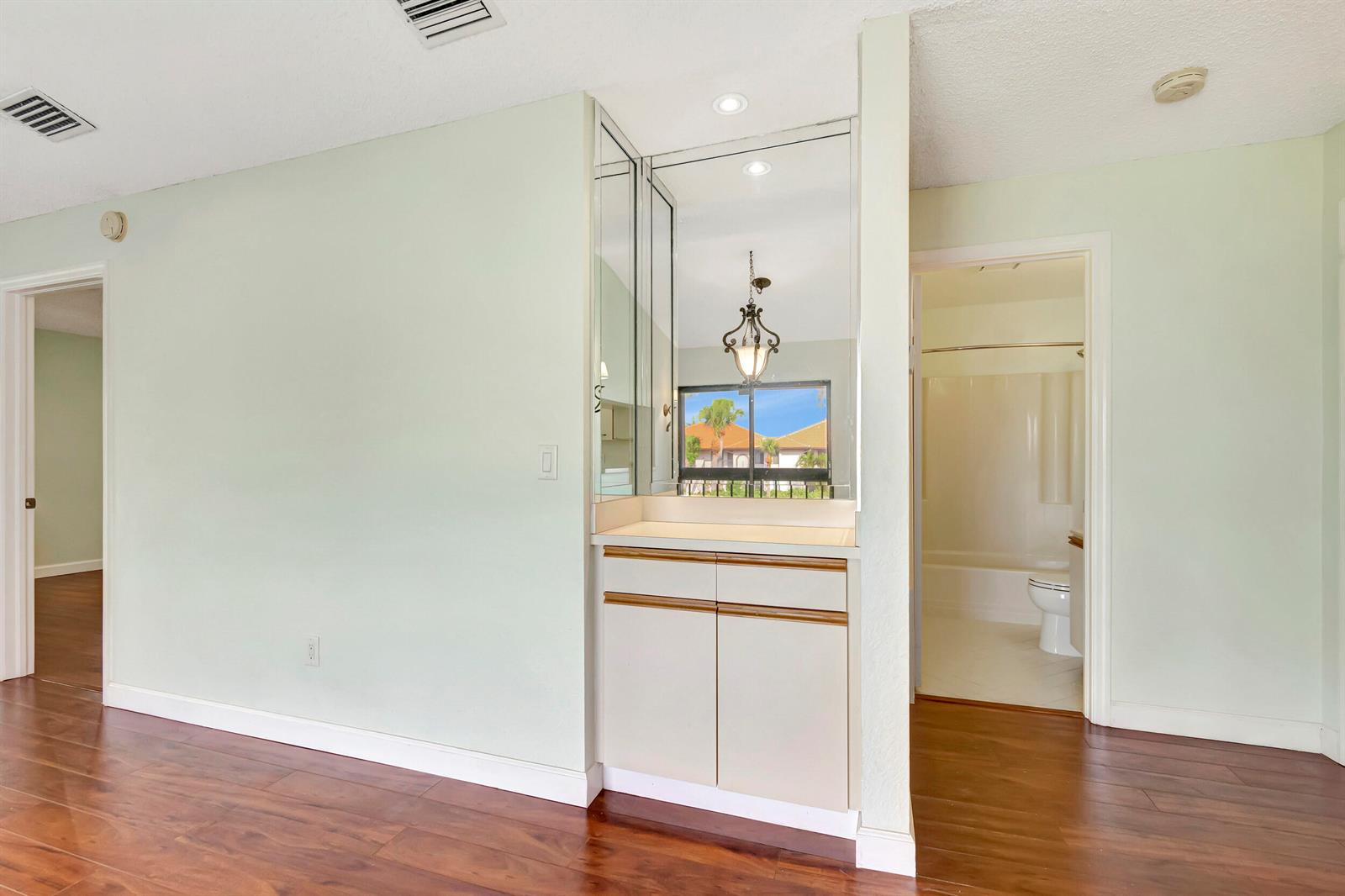 A small wet bar with mirrored walls and cabinetry sits between two doorways in a room — 351 Club Circle # 207, Boca Raton FL 33487, BOCA RATON, FL
