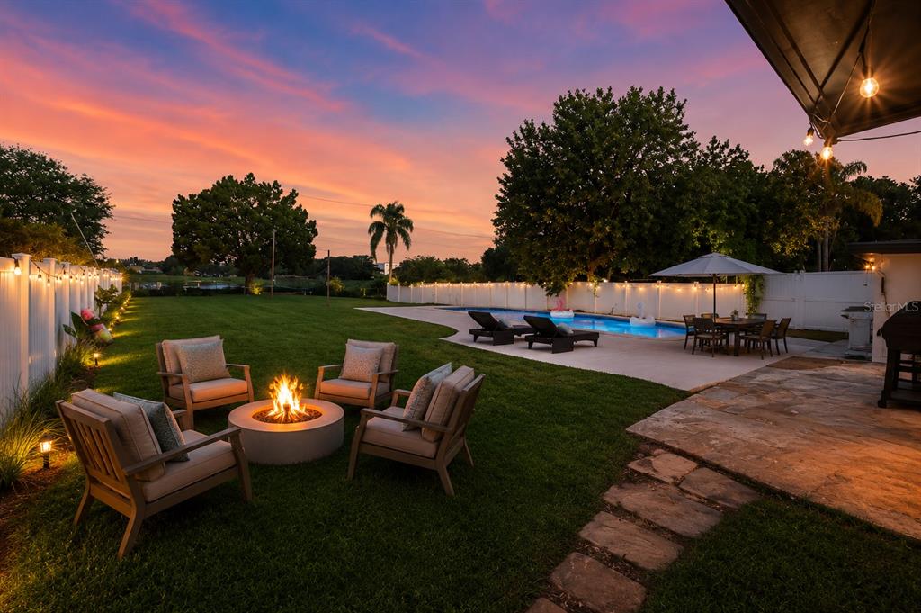 A backyard at sunset features a fire pit, seating area, swimming pool, and string lights — 8120 GONDOLA DRIVE, ORLANDO, FL
