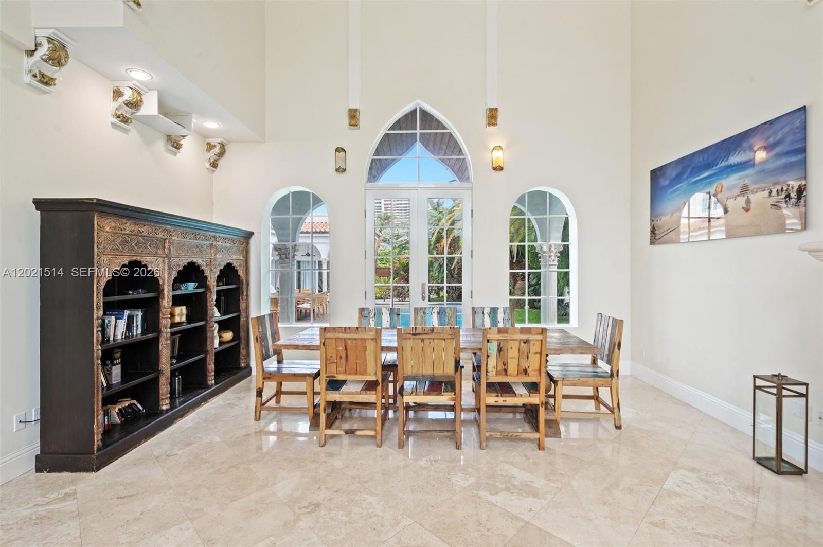 A dining room features a long wooden table, rustic chairs, and a large arched doorway — 2501 Pine Tree Dr, Miami Beach FL 33140, MIAMI BEACH, FL
