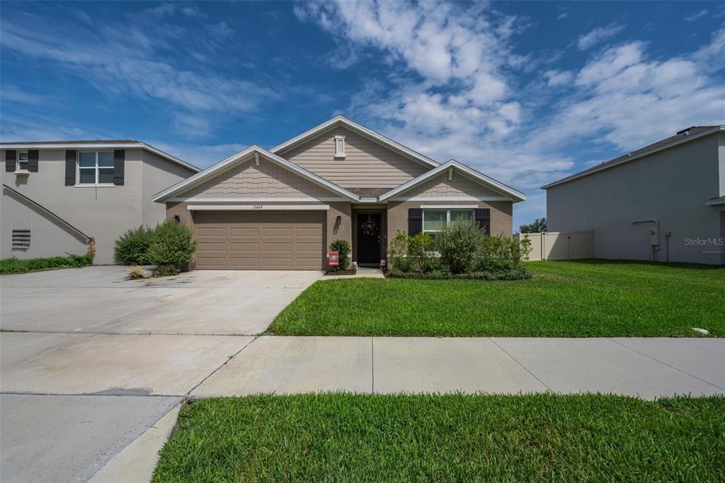 A single-story suburban house with a tan stucco exterior, a two-car garage, and a lawn — 13469 MYLION WAY, SPRING HILL, FL