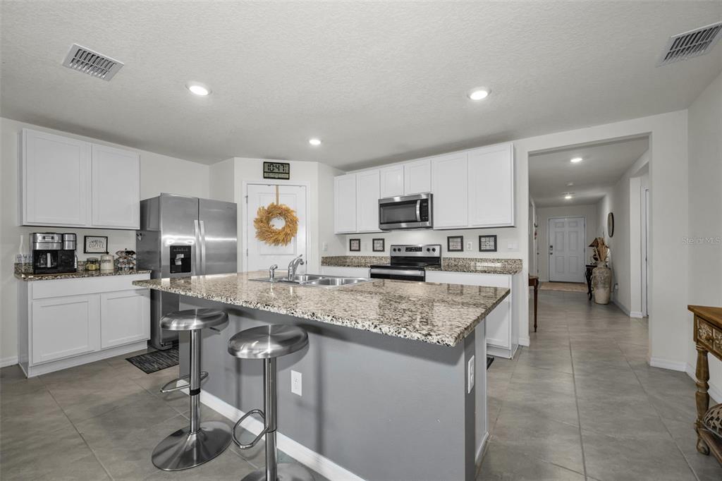 A kitchen features white cabinets, granite countertops, a central island with bar stools, and appliances — 13469 MYLION WAY, SPRING HILL, FL