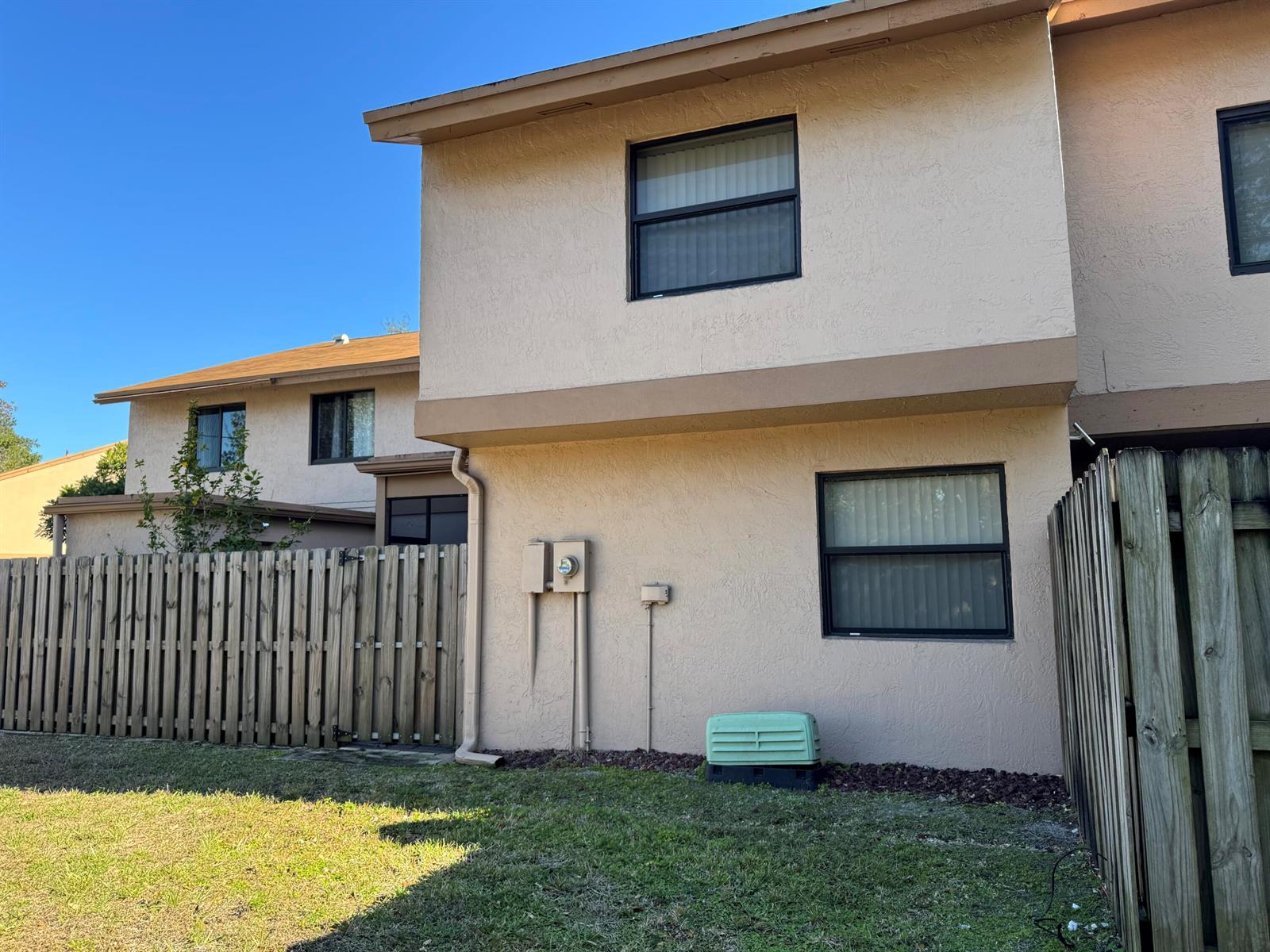 The exterior of a two-story tan stucco townhouse features a wooden fence and lawn — 31 Chestnut Circle, Cooper City FL 33026, COOPER CITY, FL