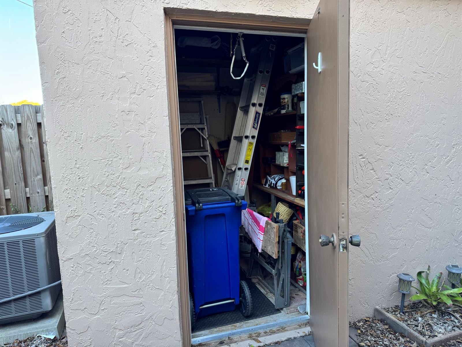 An open door reveals a cluttered storage shed containing a ladder, shelving, and a blue bin — 31 Chestnut Circle, Cooper City FL 33026, COOPER CITY, FL