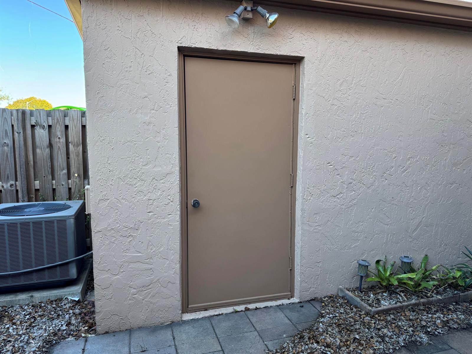 A tan metal door is set into a stucco exterior wall with a light fixture above — 31 Chestnut Circle, Cooper City FL 33026, COOPER CITY, FL