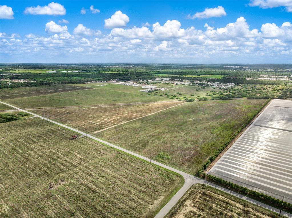 An aerial view shows a rural landscape with open fields, a road, and a greenhouse structure — 4199 DESOTO CITY ROAD, SEBRING, FL