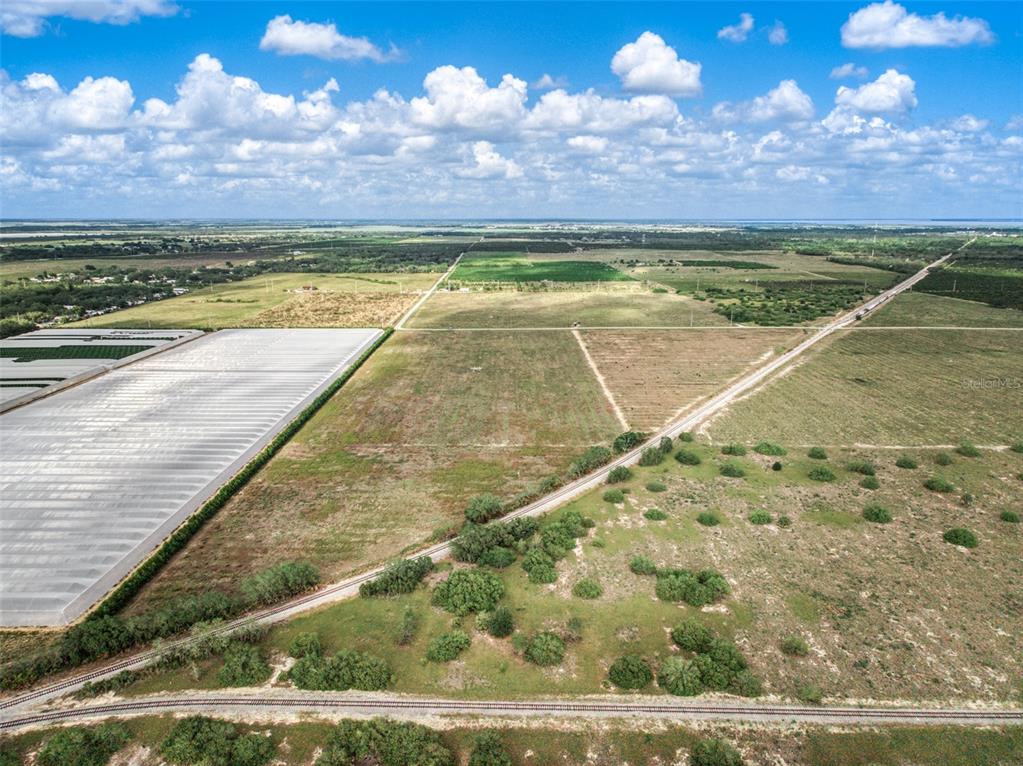 An aerial view shows a large, flat, grassy field adjacent to a greenhouse and railroad tracks — 4199 DESOTO CITY ROAD, SEBRING, FL
