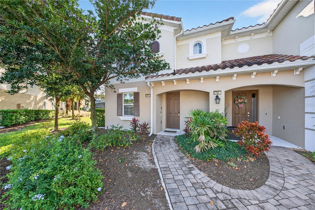 A two-story townhouse exterior with a stone walkway, landscaping, and two brown front doors — 4787 TERRASONESTA DRIVE, DAVENPORT, FL