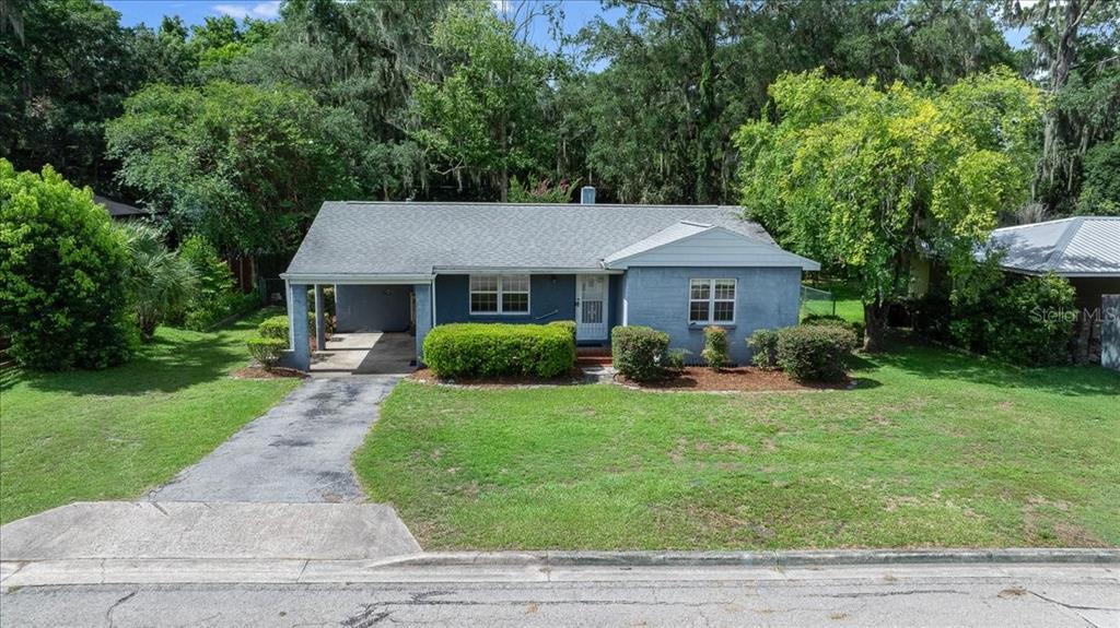 A single-story blue house with a carport and a front lawn under mature trees — 1142 NE 8TH STREET, OCALA, FL