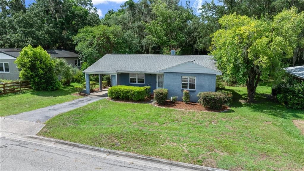 A blue, single-story house with a carport sits on a grassy lot with mature trees — 1142 NE 8TH STREET, OCALA, FL