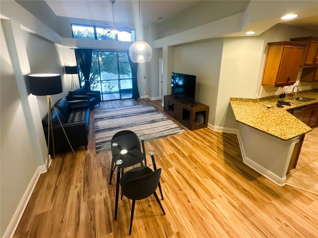 An open-concept living and dining area features wood-look flooring, a kitchen island, and sliding doors — 2543 GLORIOSA DRIVE, PALM HARBOR, FL