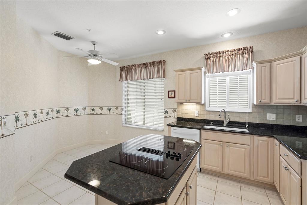A kitchen features light-colored cabinets, dark granite countertops, a center island cooktop, and tile flooring — 3954 HAMILTON CLUB CIRCLE UNIT 14, SARASOTA, FL