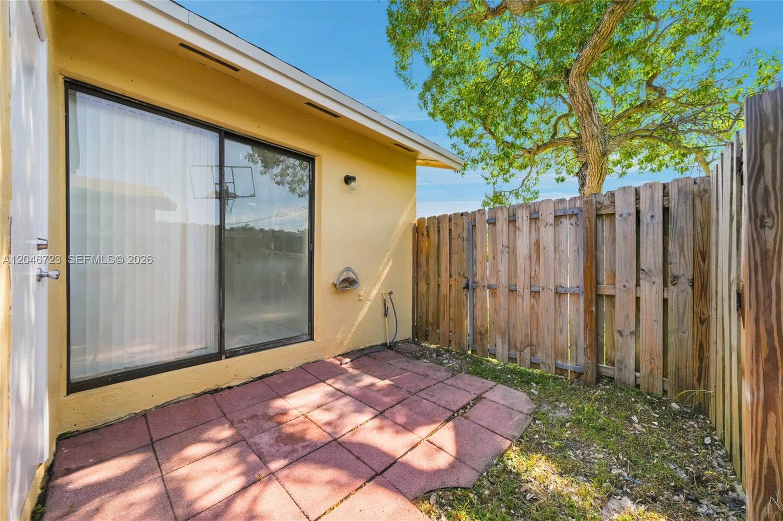 A small patio with red pavers sits next to a yellow house and wooden fence — 20117 SW 88th Ct, Cutler Bay FL 33189, CUTLER BAY, FL