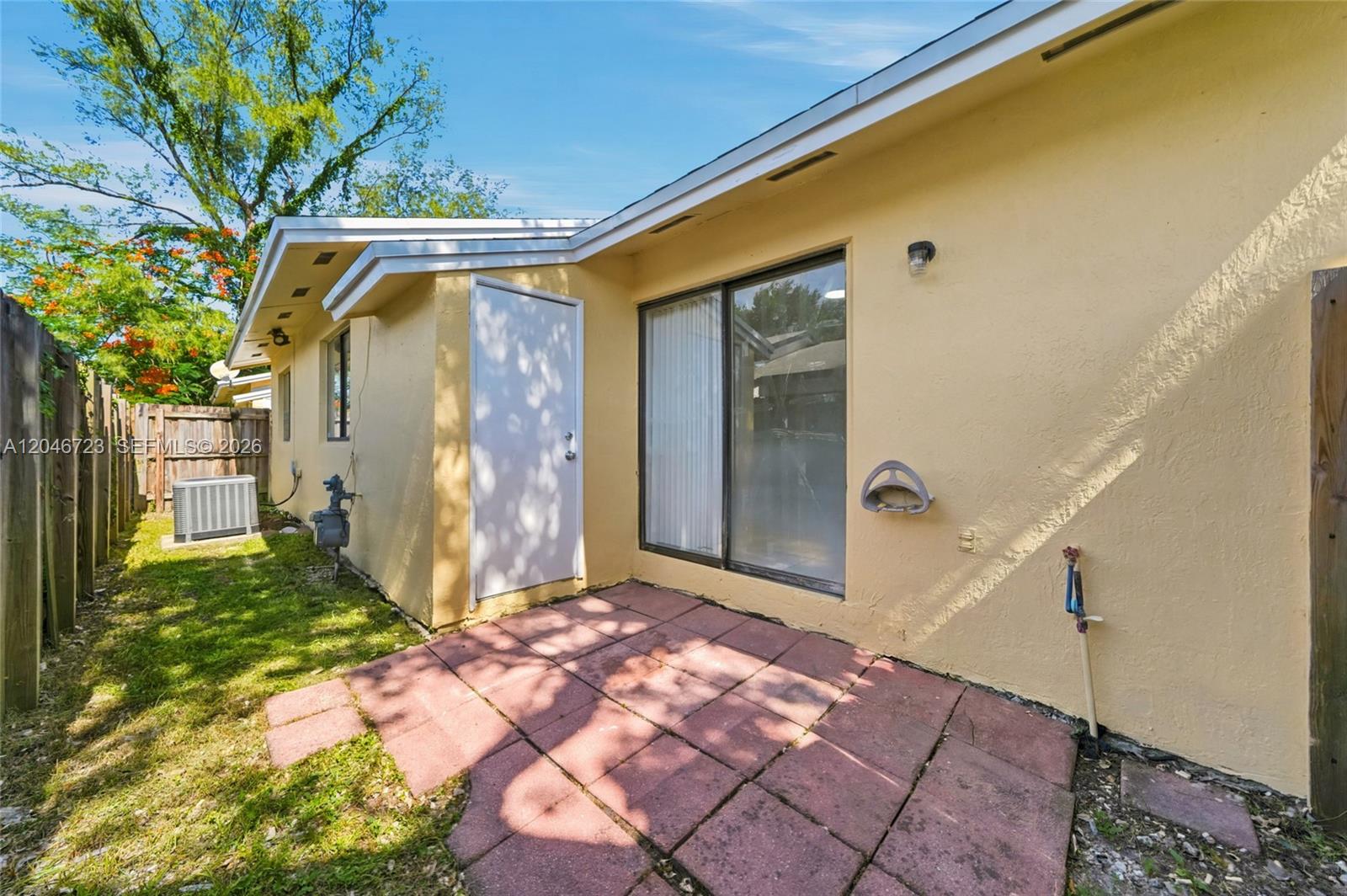 A yellow stucco house exterior features a small patio, sliding glass door, and side door — 20117 SW 88th Ct, Cutler Bay FL 33189, CUTLER BAY, FL
