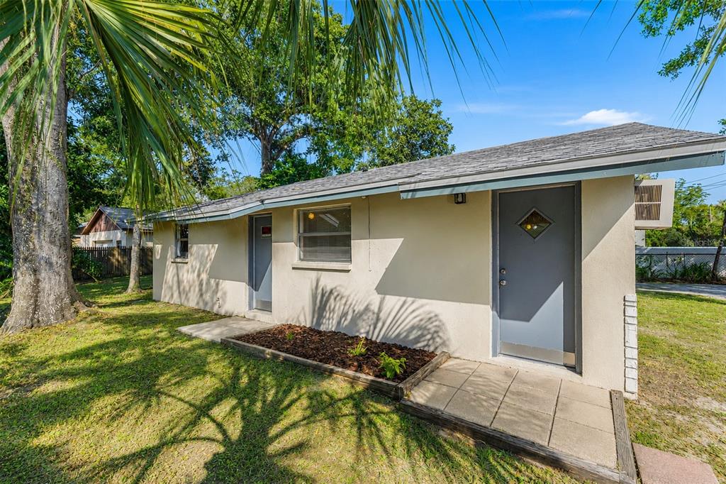 Exterior view of a single-story stucco building with two gray doors and a small garden — 9610 N 12TH STREET, TAMPA, FL