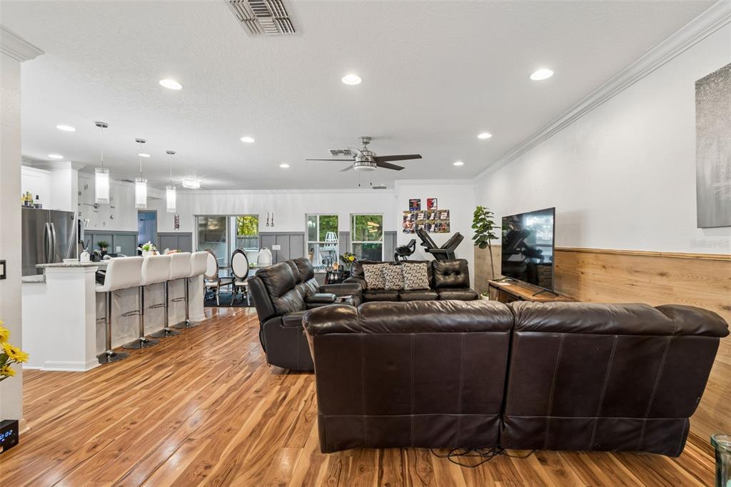 An open-concept living room features wood flooring, a leather sectional, and a kitchen breakfast bar — 13046 LINDEN DRIVE, SPRING HILL, FL