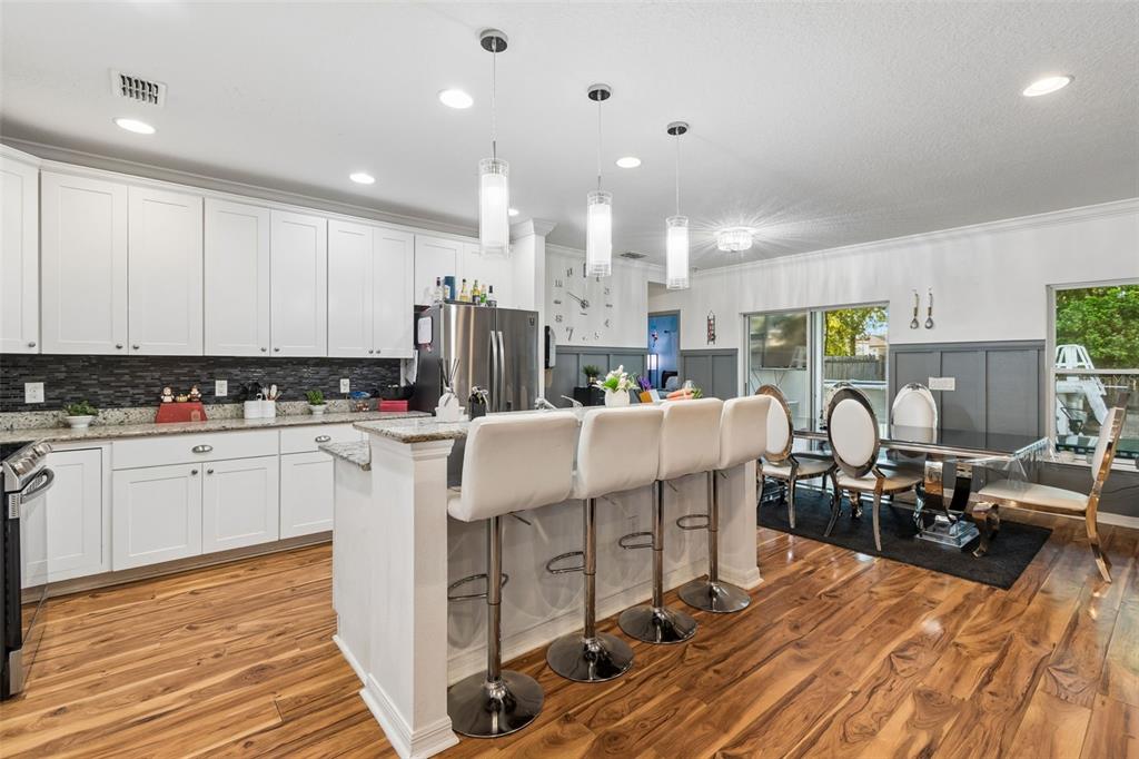 A kitchen with white cabinets, a granite-topped island, and bar stools next to a dining area — 13046 LINDEN DRIVE, SPRING HILL, FL