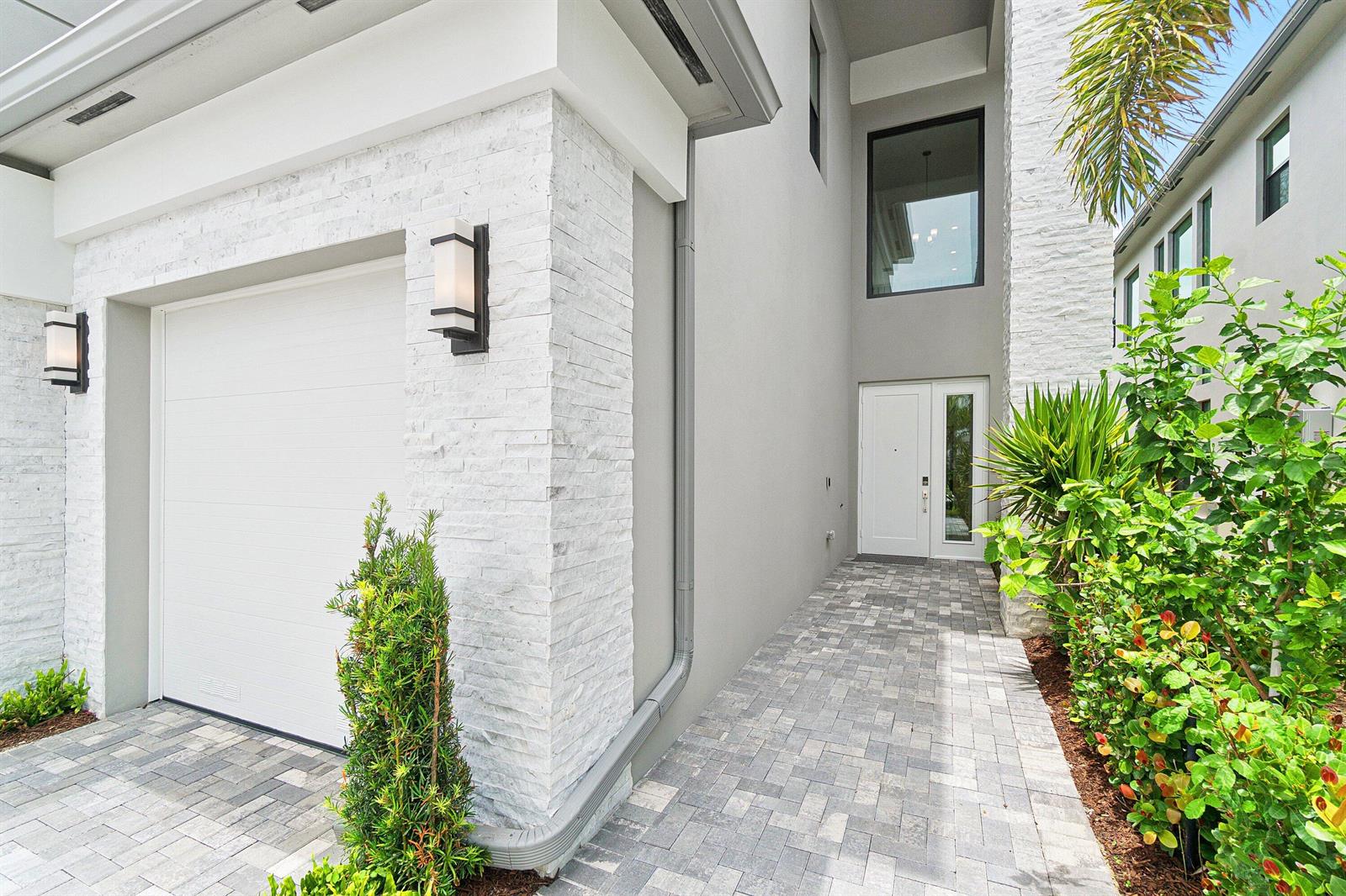 The exterior of a modern home features white stone accents, a garage, and a walkway — 9241 Sunflower Meadow Road, Boca Raton FL 33434, BOCA RATON, FL
