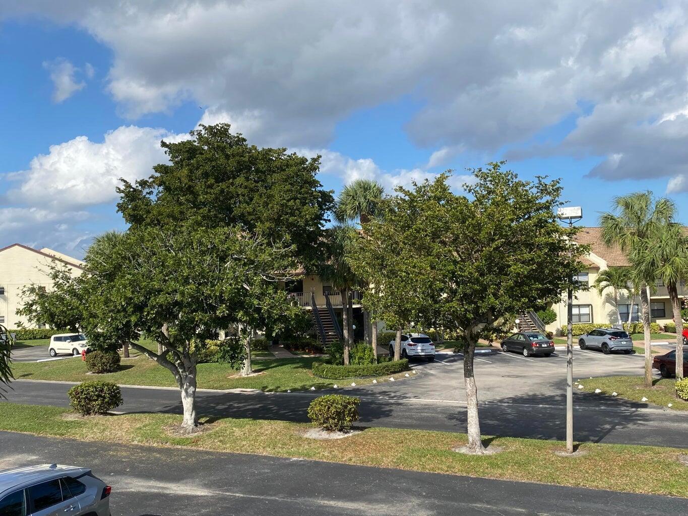 An exterior view of a multi-story apartment building with parking, trees, and a blue sky — 7915 Willow Spring Drive # 1223, Lake Worth FL 33467, LAKE WORTH, FL