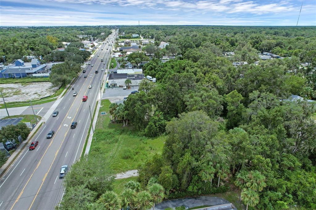 An aerial view shows a vacant, tree-covered lot adjacent to a multi-lane highway — S VOLUSIA AVENUE, ORANGE CITY, FL