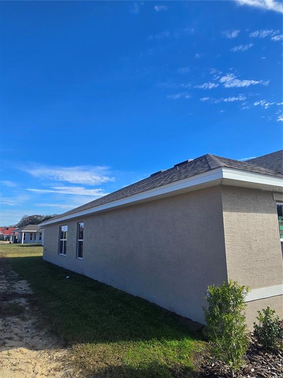 The exterior side view of a tan stucco house features a shingled roof and windows — 1100 HERON POINT DRIVE, INVERNESS, FL
