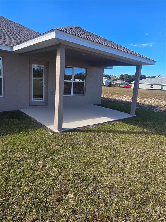 A covered concrete patio extends from the rear of a tan stucco house — 1100 HERON POINT DRIVE, INVERNESS, FL